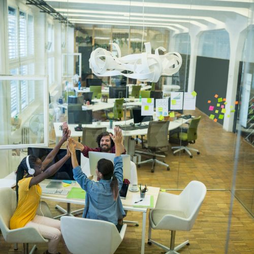 Group of graphic designers giving high five to each other in office